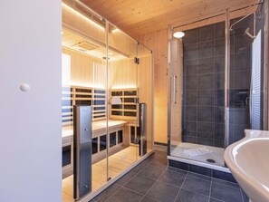 A modern bathroom with a glass-enclosed shower, a wooden sauna, and a white sink. - One-bedroom Cabin (Sankt Georgen am Kreischberg)