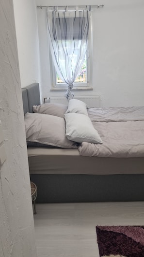 A bed with pillows, a window with curtains, and a radiator. - At home in Oppenheim (Oppenheim)