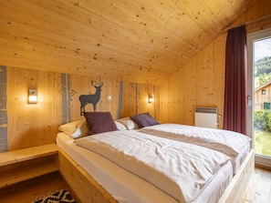 A wooden cabin bedroom with a bed, pillows, a wall-mounted deer silhouette, and a window with a view of greenery. - One-bedroom Cabin (Sankt Georgen am Kreischberg)