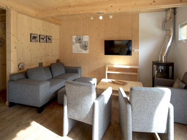 A modern living room with a sectional sofa, a flat-screen TV, and a wood-burning stove. - One-bedroom Cabin (Sankt Georgen am Kreischberg)