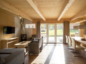 A modern interior with a wooden ceiling, a flat-screen TV, a dining area with chairs, and a view through the glass doors. - One-bedroom Cabin (Sankt Georgen am Kreischberg)