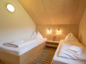 A room with two beds, wooden walls, a sloped ceiling, and two wall-mounted lights. - One-bedroom Cabin (Sankt Georgen am Kreischberg)