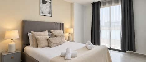 A hotel room with a large bed, two bedside tables, a wall-mounted picture, and a window with curtains.