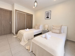 Habitación de hotel con dos camas, un armario, una mesita de noche con lámpara y un cuadro en la pared.