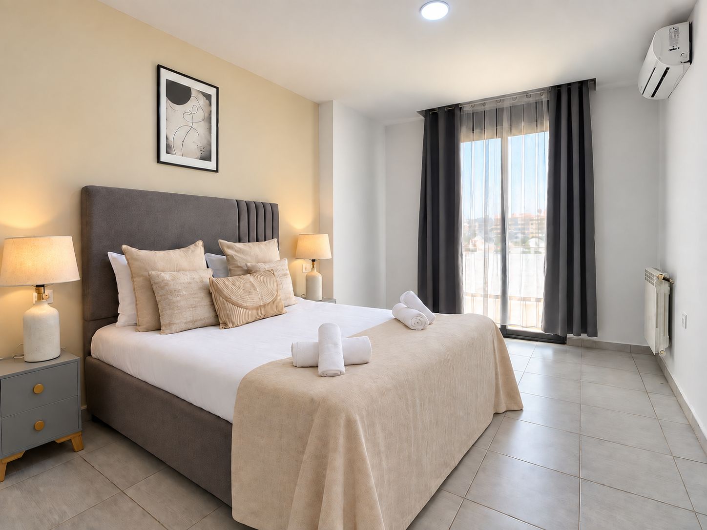 A hotel room with a bed, two bedside lamps, a window with curtains, and a radiator.