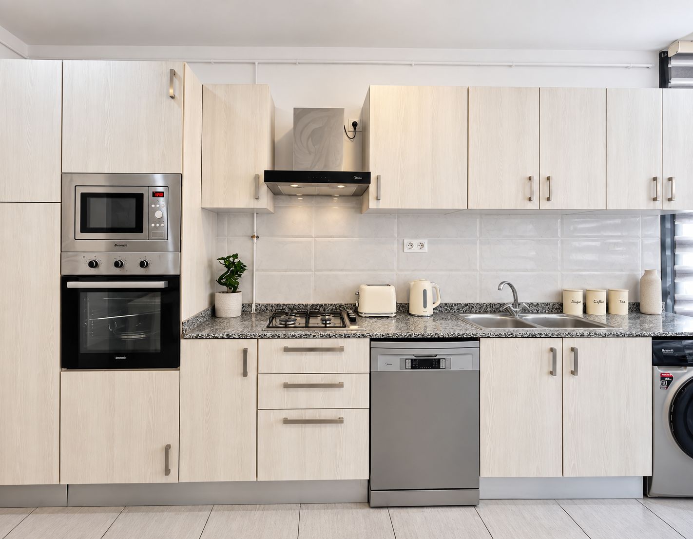 A modern kitchen with stainless steel appliances, light wood cabinetry, and a granite countertop.