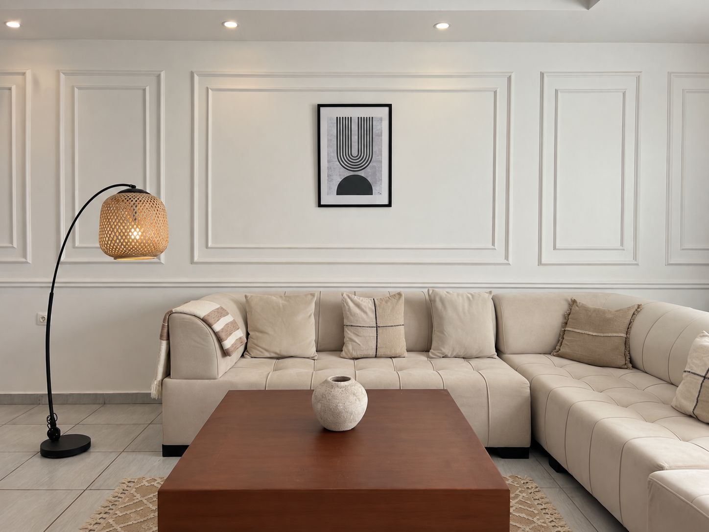 A modern living room with a beige sectional sofa, a wooden coffee table, a floor lamp, and a framed abstract artwork on the wall.