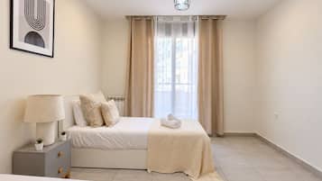 A modern bedroom with a bed, bedside tables, a lamp, and a window with curtains.