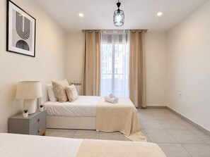 Quarto moderno com cama, mesas de cabeceira, abajur e janela com cortinas.