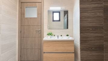 Un baño con puerta de madera, un espejo sobre un lavabo blanco y una ventana pequeña.