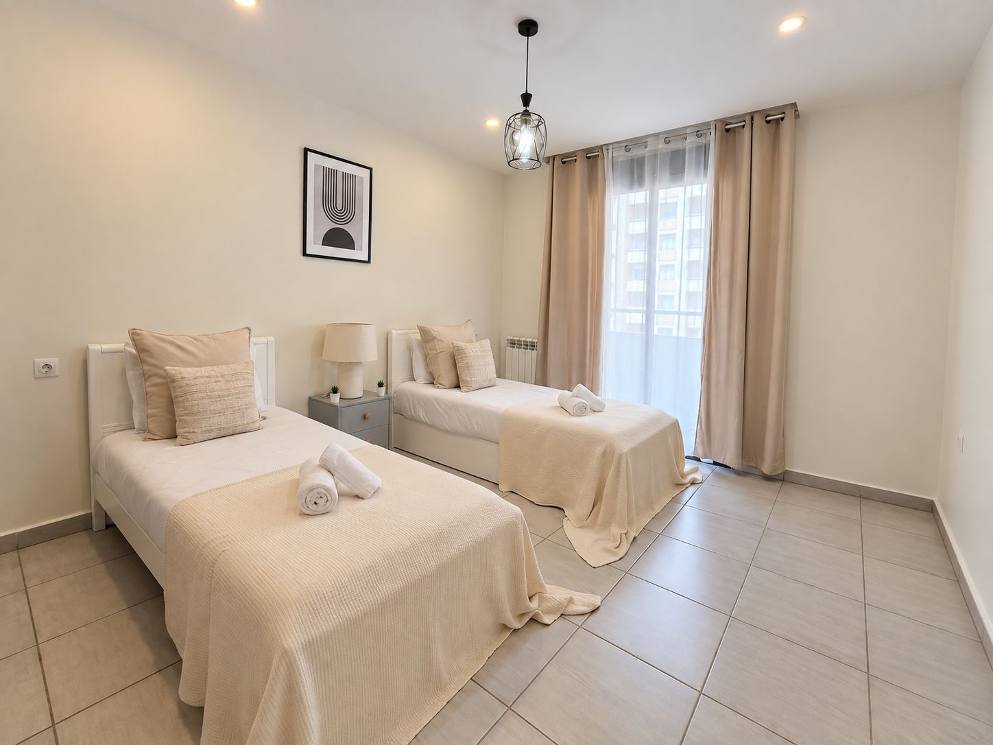 Une chambre d’hôtel avec deux lits, une table de chevet avec une lampe, un tableau encadré au mur et une fenêtre avec des rideaux.