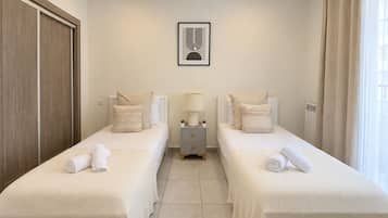 A hotel room with two beds, a nightstand with a lamp, a framed picture on the wall, and a window with curtains.