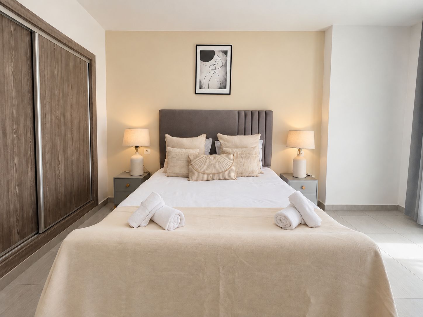 Habitación de hotel con una cama grande, dos mesitas de noche con lámparas, un armario y una obra de arte enmarcada en la pared.