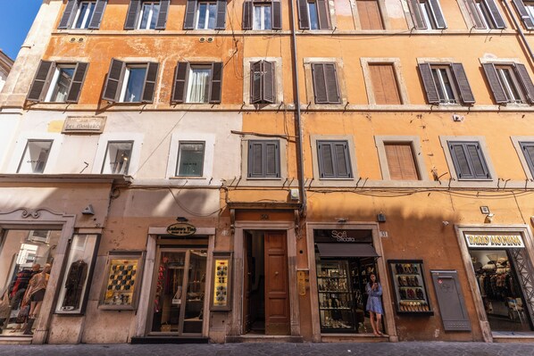 Une rangée d’immeubles à étages, dotés de devantures de magasins, parmi lesquels on trouve une boutique de chaussures et une boutique de vêtements.