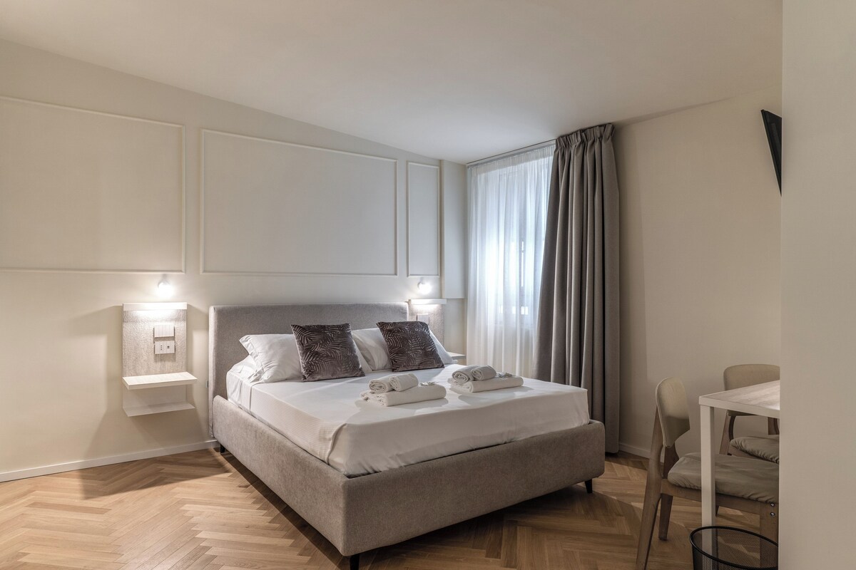 A hotel room with a bed, bedside lamps, a desk, and a chair.