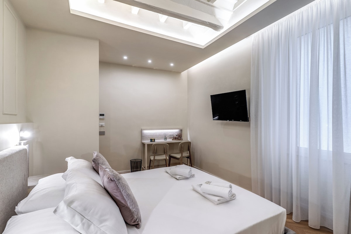 A hotel room with a bed, a desk, a chair, a TV, and a window with curtains.