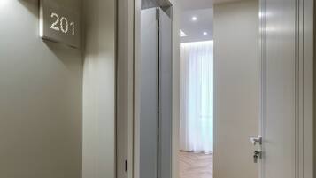 Un couloir avec une porte portant l’inscription « 201 », qui donne sur une pièce dotée d’une grande fenêtre et d’un rideau.