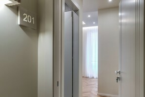 Un pasillo con una puerta marcada '201' que da a una habitación con un ventanal y una cortina.