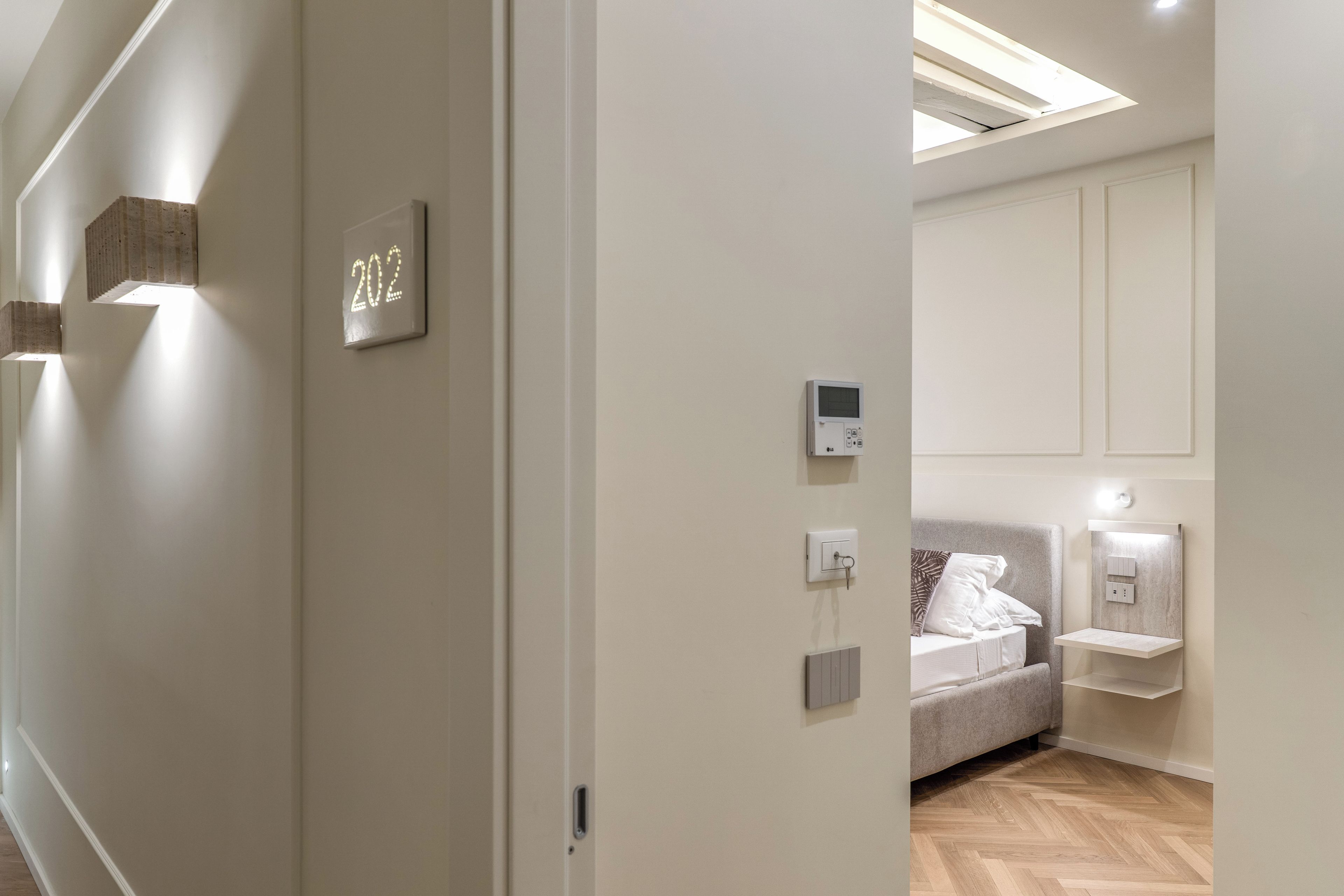 Une chambre d’hôtel équipée d’un lit, de tables de chevet, d’un thermostat fixé au mur et d’un panneau indiquant le numéro de chambre, soit le 202.