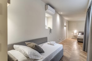 Un dormitori modern amb un llit, aire condicionat fixat a la paret, un mirall i una petita planta en test.