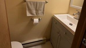 Un baño pequeño con inodoro, lavamanos, espejo, toallero y un calentador.