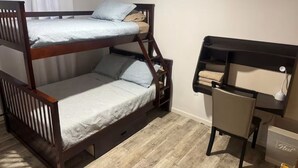 Una cama litera con escritorio y silla, una ventana con cortinas, y suelo de madera.