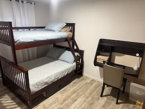 Een stapelbed met een bureau en stoel, een raam met gordijnen en een houten vloer.