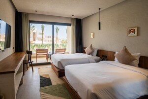 Habitación de hotel con dos camas, un escritorio y vistas a palmeras y edificios.
