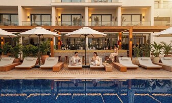 Un área junto a la piscina con sillones de descanso y sombrillas, un bar y una piscina reflectante.