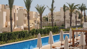 A rooftop pool area with lounge chairs and umbrellas, surrounded by palm trees and buildings.
