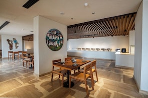 A dining area with wooden tables and chairs, a large wall painting, and a kitchen area with a long counter.