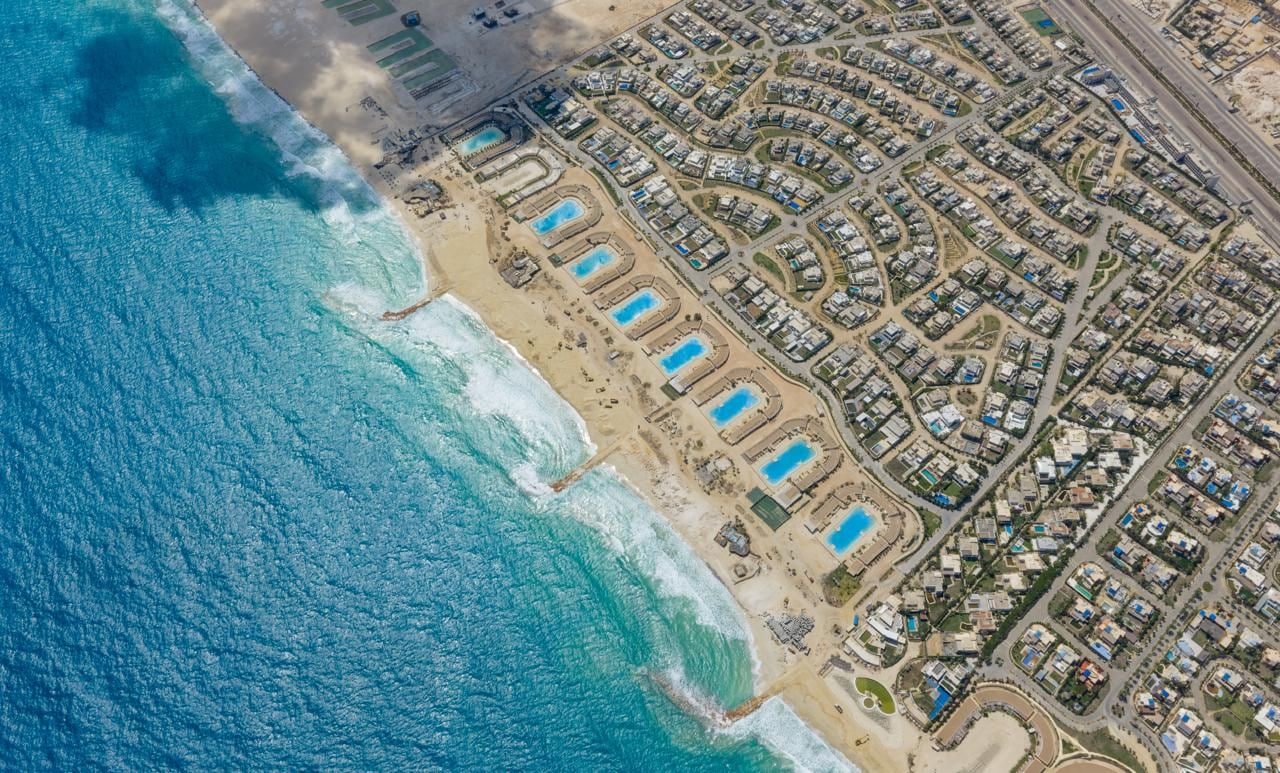 Vista aérea de una zona residencial costera con playa, piscinas y un conjunto denso de casas.