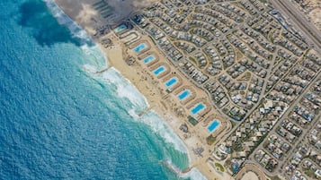 Vista aérea de una zona residencial costera con playa, piscinas y un conjunto denso de casas.