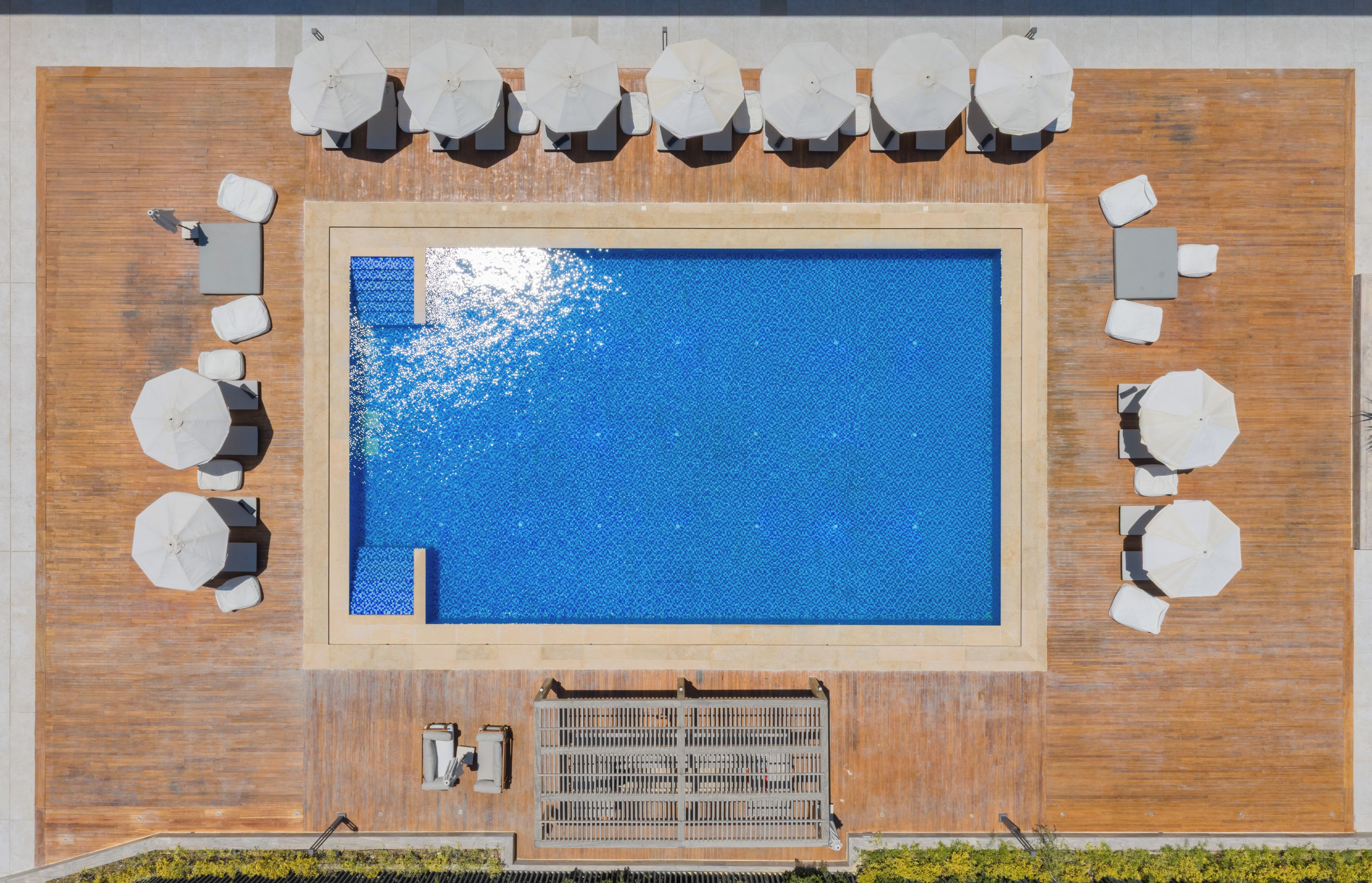 Una piscina en la azotea con una terraza de madera, rodeada de sombrillas blancas y sillones de descanso.