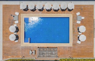 Una piscina en la azotea con una terraza de madera, rodeada de sombrillas blancas y sillones de descanso.