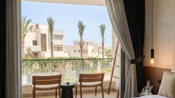 A hotel room with a bed, a balcony with chairs, and a view of buildings.