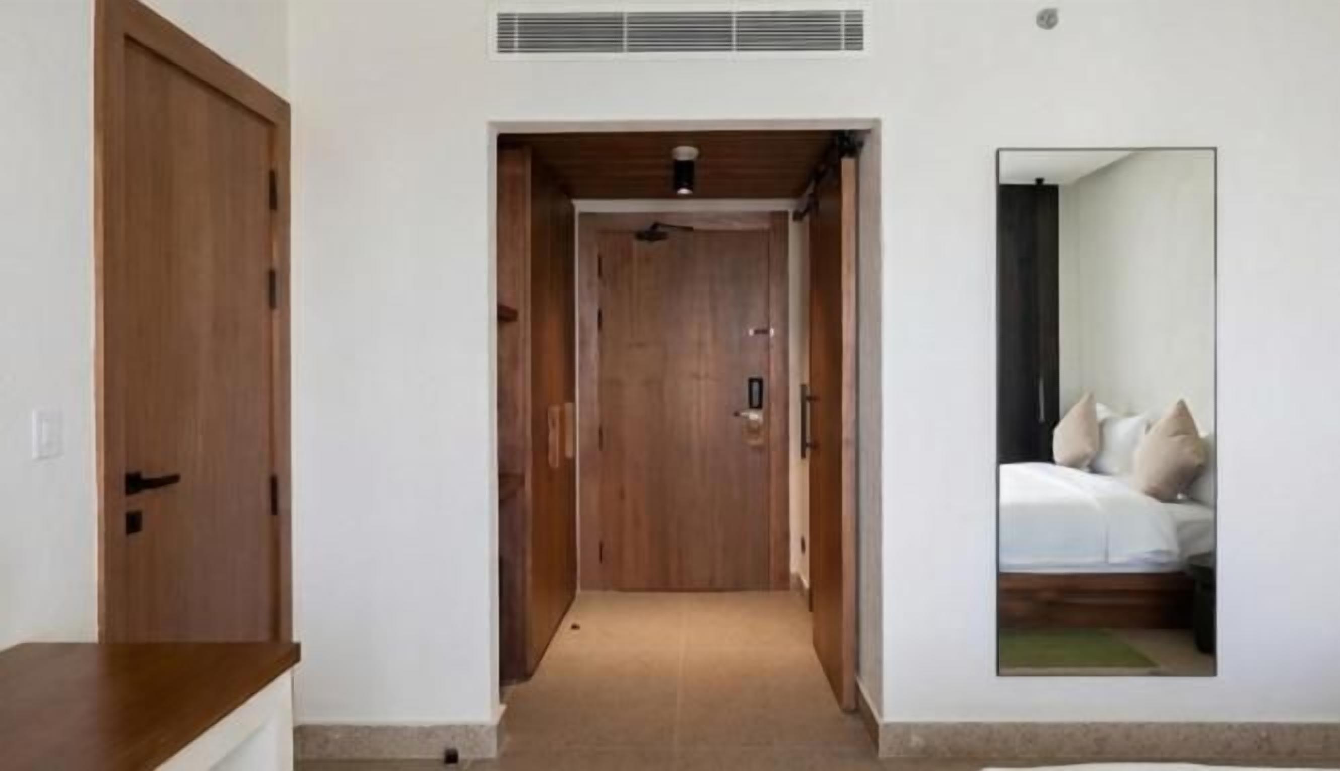 Un pasillo que da a un dormitorio con una cama y un espejo que refleja la habitación.
