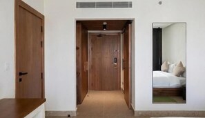 A hallway leading to a bedroom with a bed and a mirror reflecting the room.