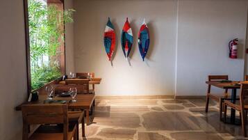 Un área de comedor con mesas y sillas de madera, un extintor en la pared y tres tablas de surf coloridas montadas en la pared.