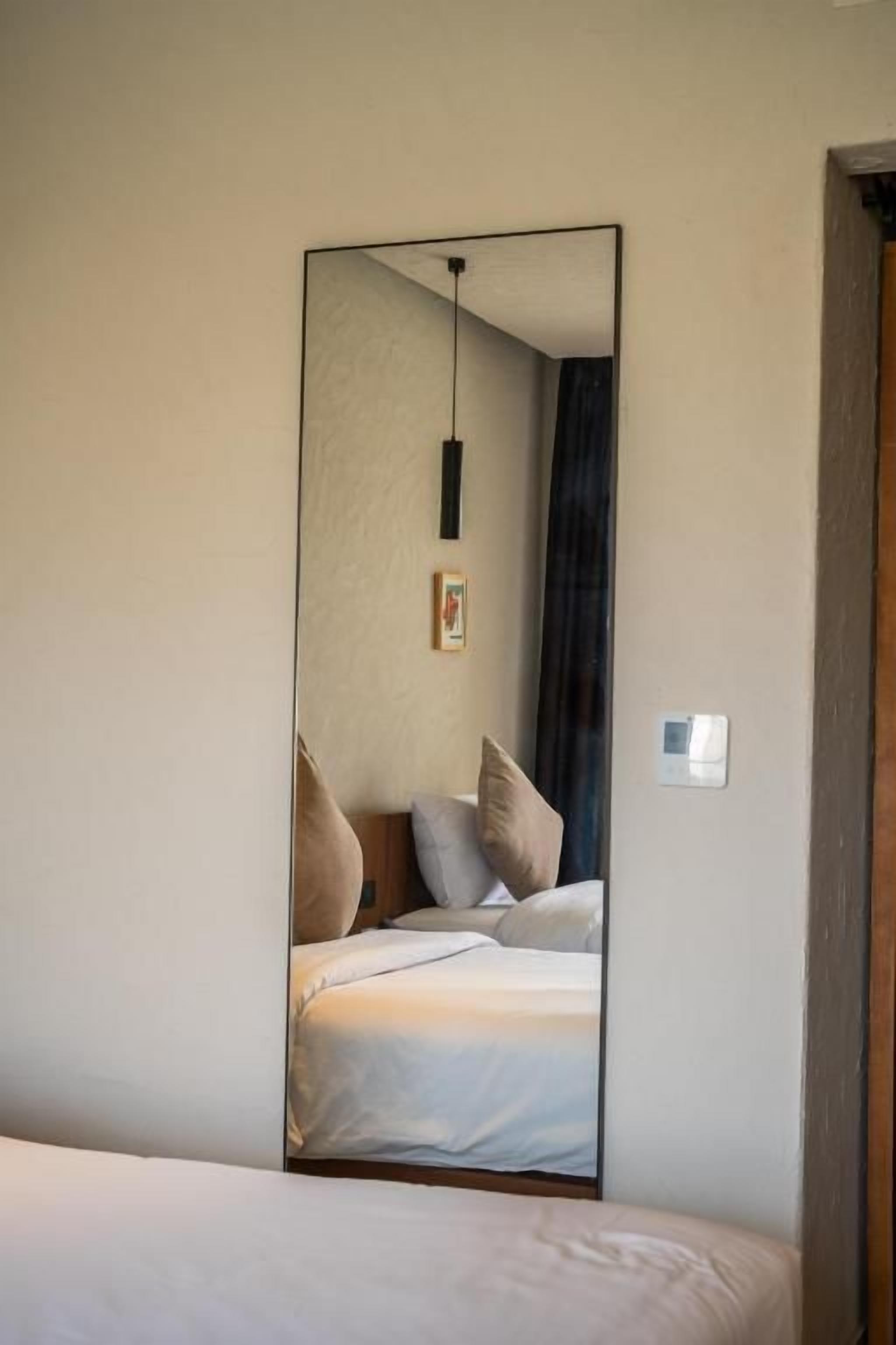 A bedroom with a large mirror reflecting a bed, a hanging light fixture, and a framed picture on the wall.