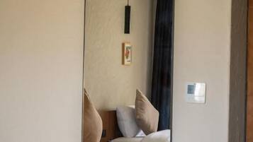 A bedroom with a large mirror reflecting a bed, a hanging light fixture, and a framed picture on the wall.