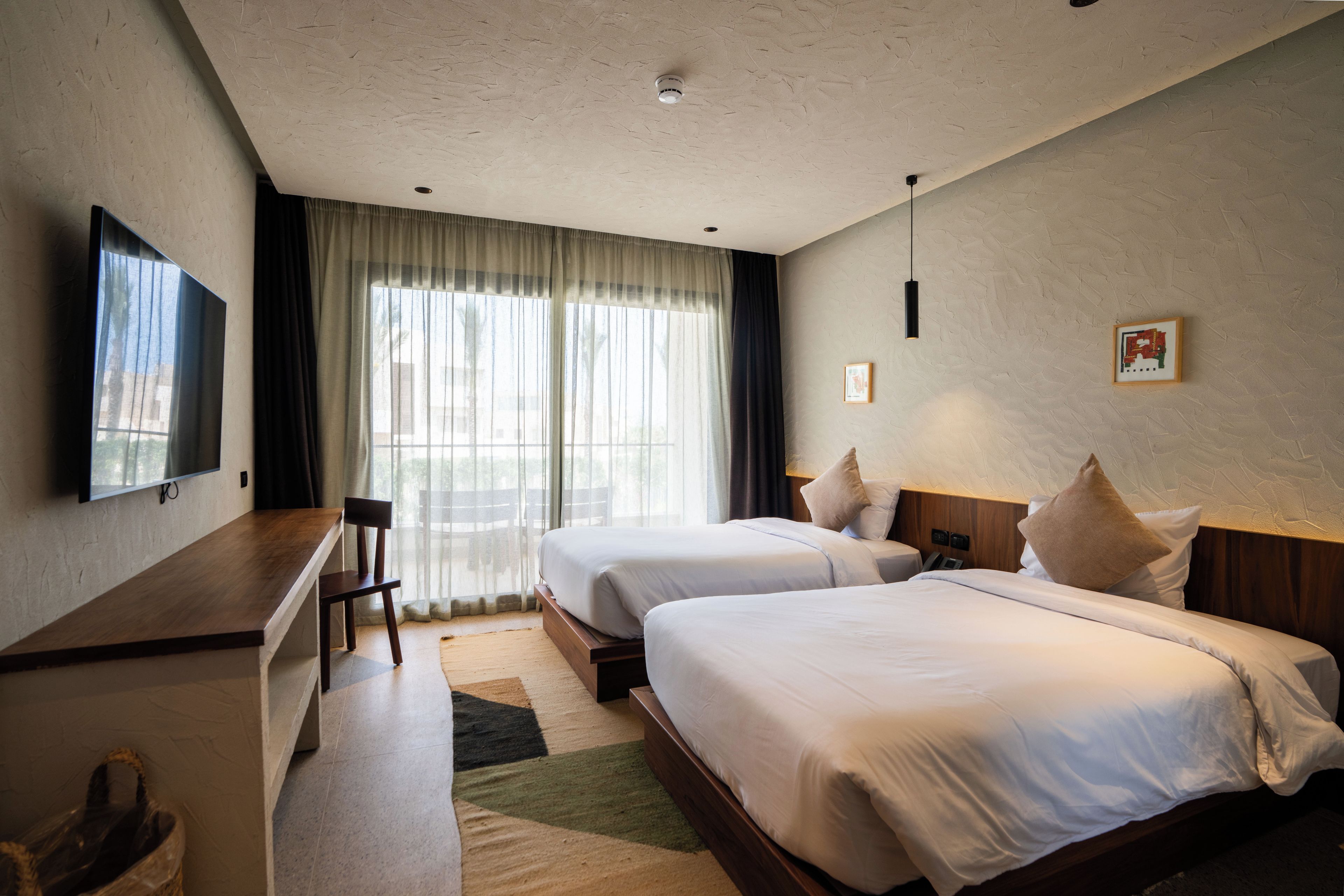 Habitación de hotel con dos camas, un escritorio, una silla, un televisor y una ventana con cortinas.