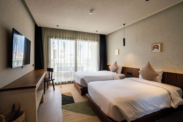 A hotel room with two beds, a desk, a chair, a TV, and a window with curtains.