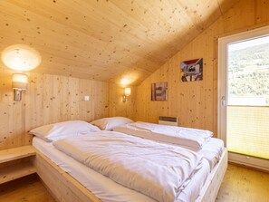 Ein Schlafzimmer einer Holzhütte mit zwei Betten, einem Fenster mit Blick ins Freie und einer Wandlampe.