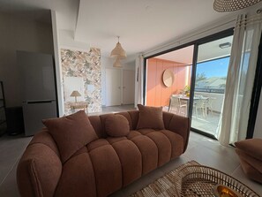 Ein modernes Wohnzimmer mit einer Eckcouch, einem Essbereich mit Gartenmöbeln und einer großen Schiebeglastür, die auf einen Balkon führt.