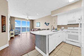 A modern kitchen with white cabinetry, a dining area with a view, and a balcony with a view. - Celadon 1505 - Turquoise Oasis (Panama City Beach)