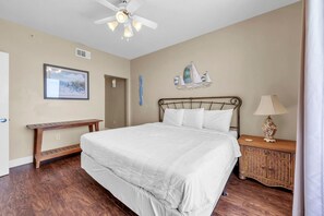 Un dormitorio con cama, mesita de noche, banqueta, ventilador de techo y decoración en la pared.