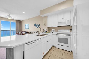 A modern kitchen with a large island, white cabinetry, and a view of the ocean. - Celadon 1505 - Turquoise Oasis (Panama City Beach)