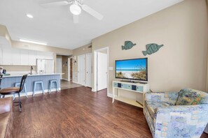 Una sala de estar moderna con un televisor de pantalla plana, un sofá y una zona de cocina con armarios blancos y una barra.