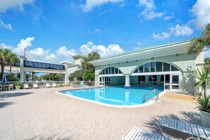 Una piscina con área techada, un puente peatonal y palmeras.